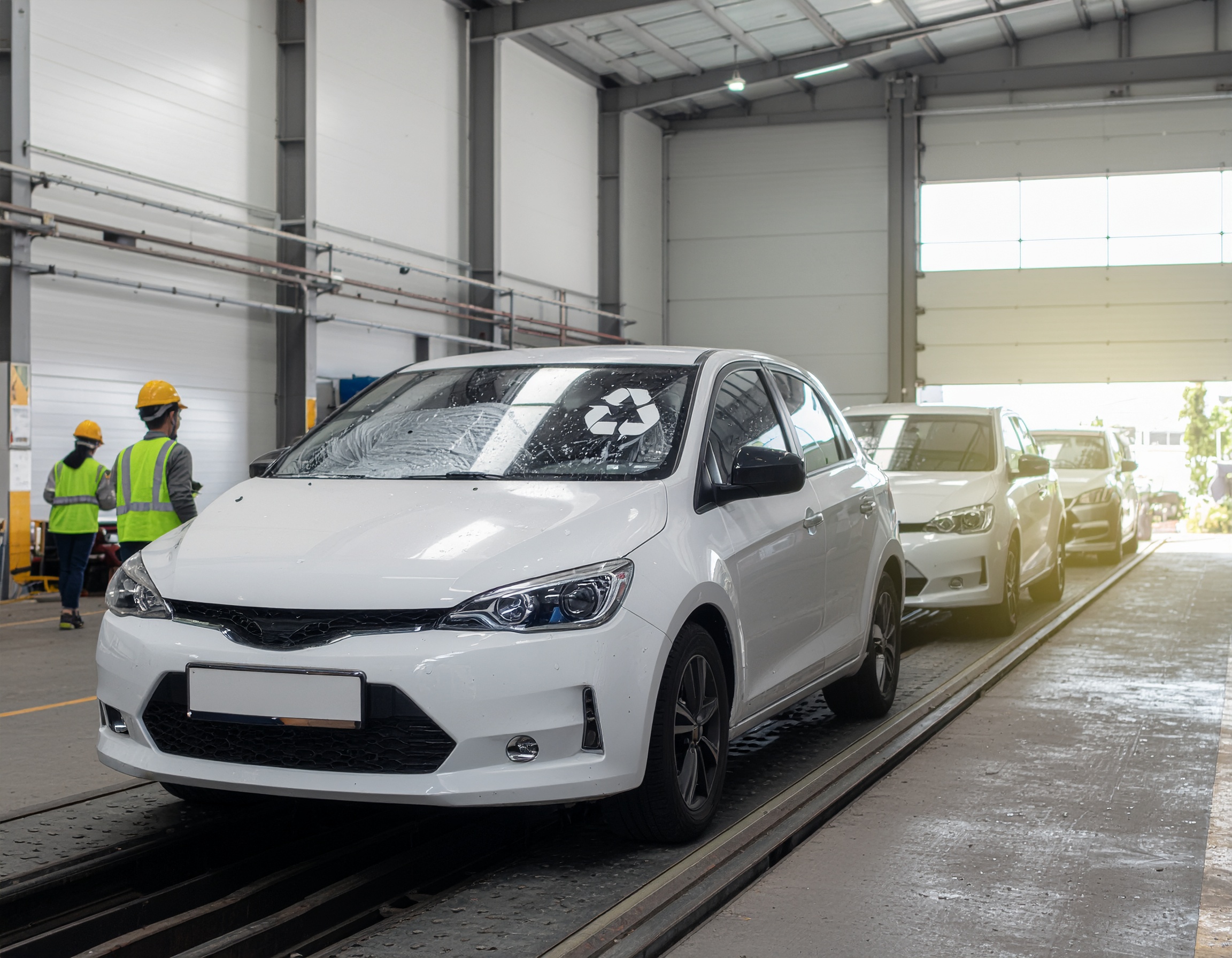 Firefly" fleet vehicles at a recycling facility. White cars lined up, ready for sustainable processing. Workers wearing safet